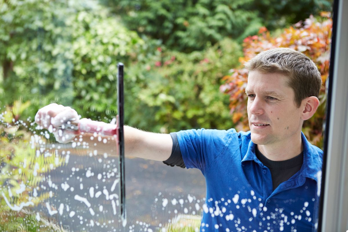 A man using a squeegee to clean a large window, ensuring a clear and spotless surface.