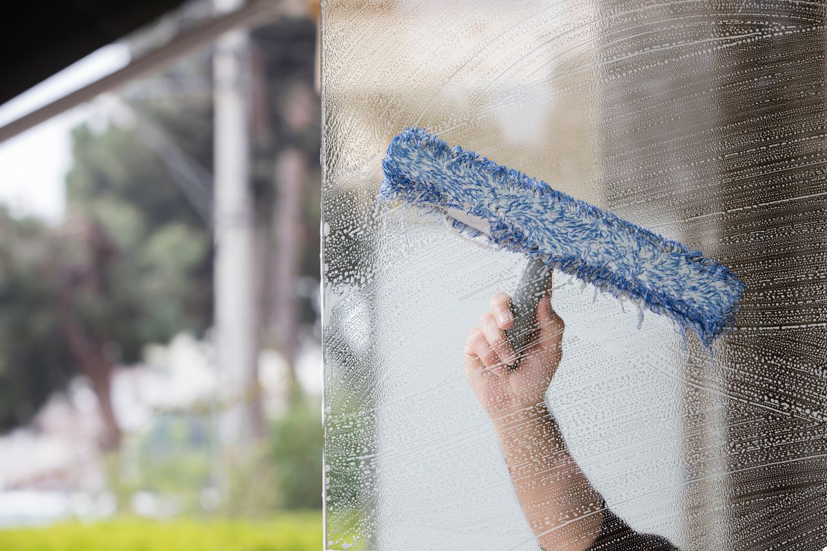 A person using a blue brush to clean a window, ensuring a clear and spotless surface.