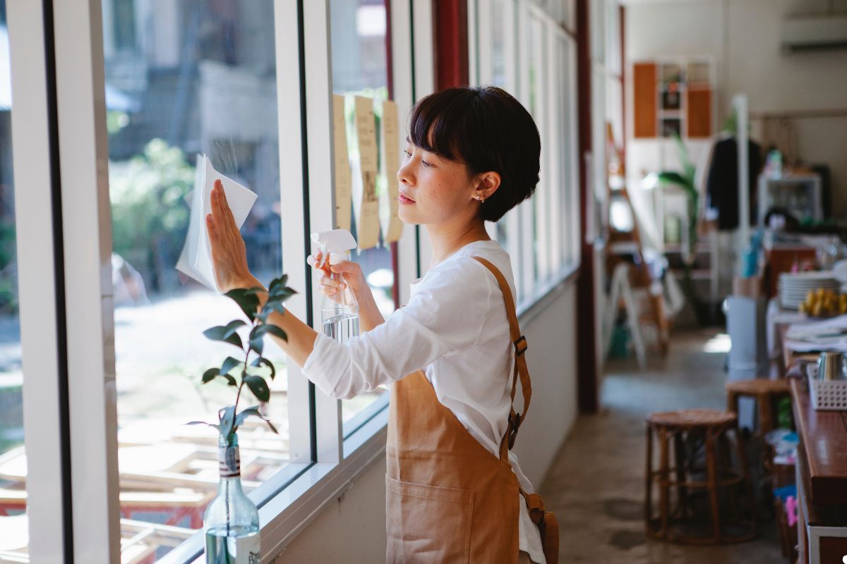 A woman using a cloth to clean a large window in a retail store, ensuring a clear view for customers.